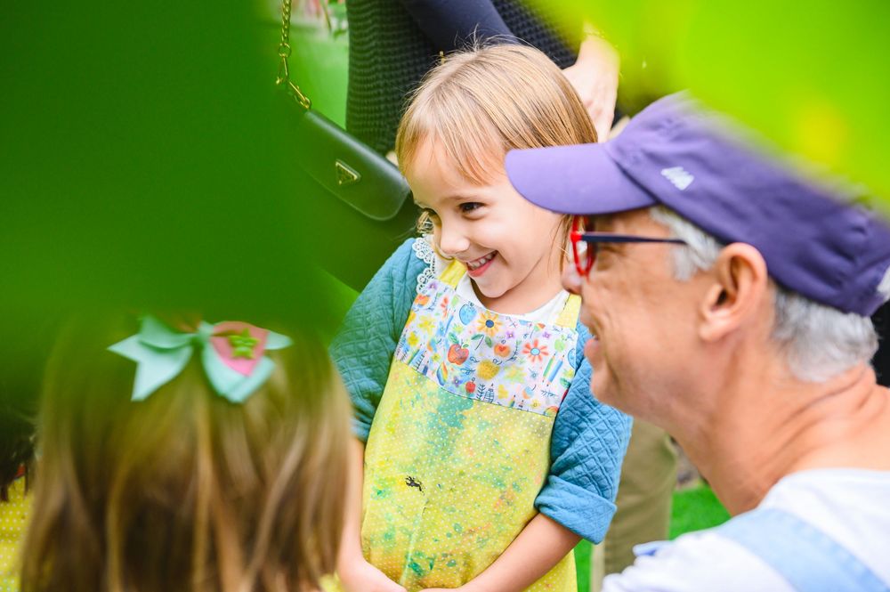 Educator guides outdoor learning activities with young students in lush green garden environment.