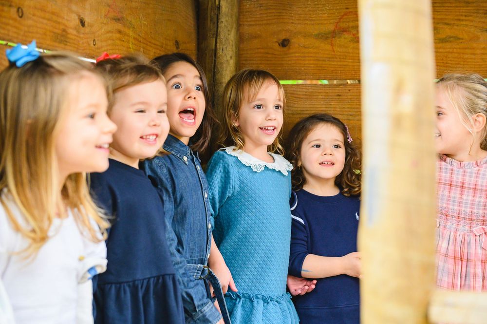 A group of children in casual dress stand close together and laugh while posing against a wooden wall.