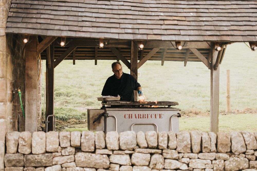 A rustic outdoor covered patio area with wooden beams, stone walls and countryside views in the background.