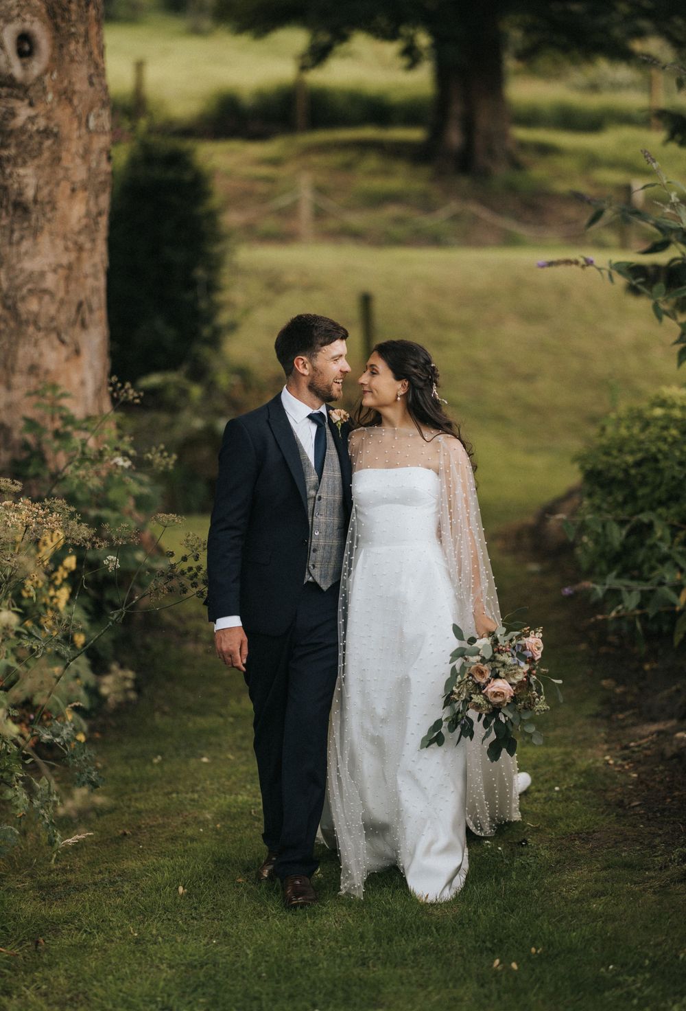 A couple shares an intimate moment on their wedding day in a lush garden setting with trees and greenery.