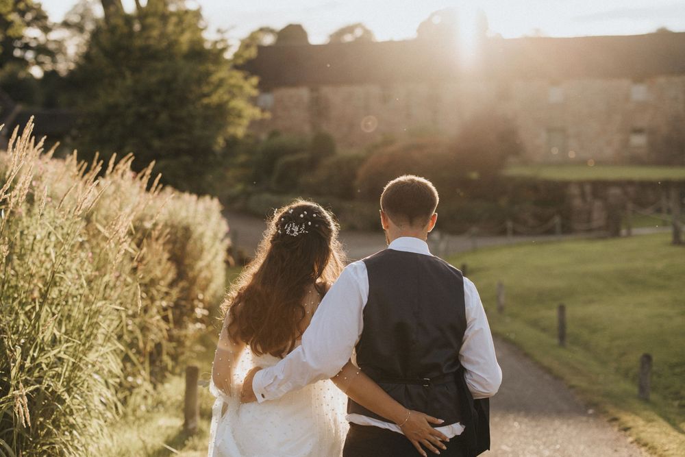 A couple walks hand in hand along a garden path at sunset with golden light illuminating tall ornamental grasses.