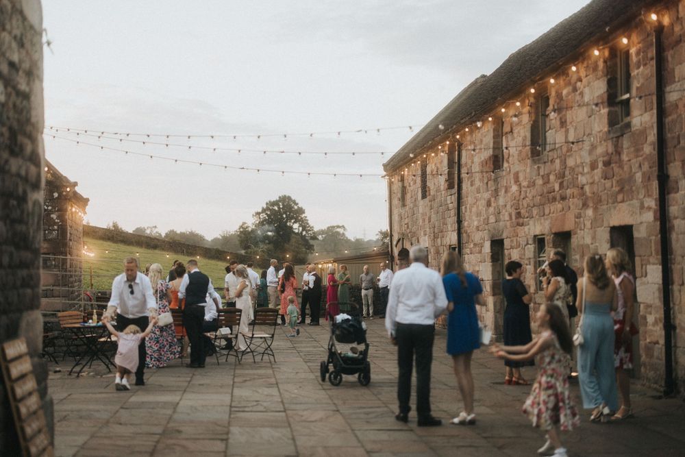 Wedding reception at rustic stone venue with twinkle lights and guests mingling on outdoor patio.