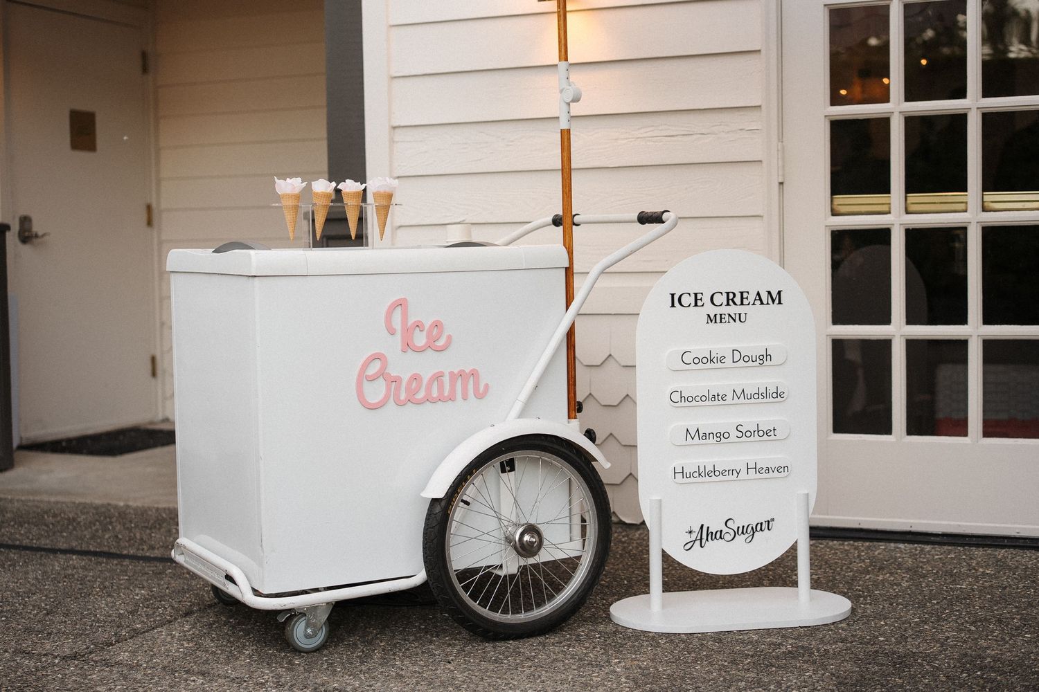A white ice cream cart parked against a white building exterior with windows and glass doors.
