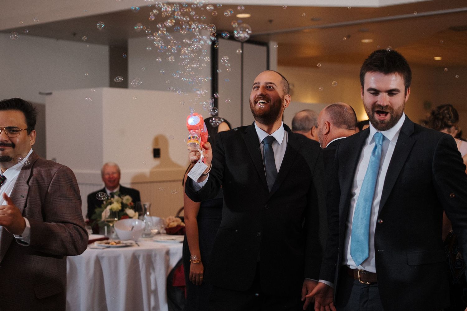 Guests in formal attire attend an elegant indoor gathering with soft lighting and festive decorations.