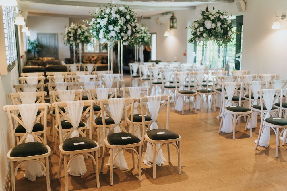 Elegant wedding reception venue with rustic wooden chairs, white floral arrangements, and warm ambient lighting.