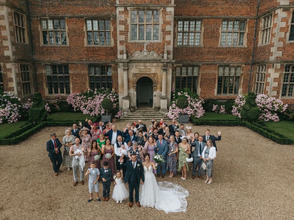 Wedding party and guests gathered in the courtyard of a historic Tudor-style brick building.