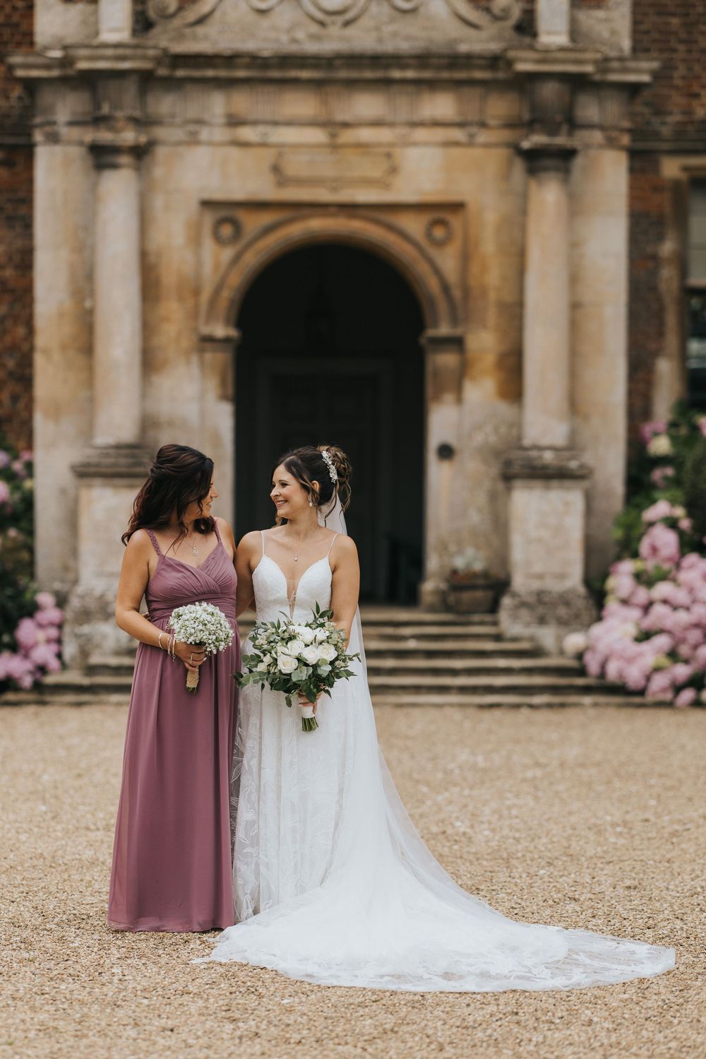 Beautiful wedding photo outside historic stone building entrance with flowing white gown and dusty rose bridesmaid dress.