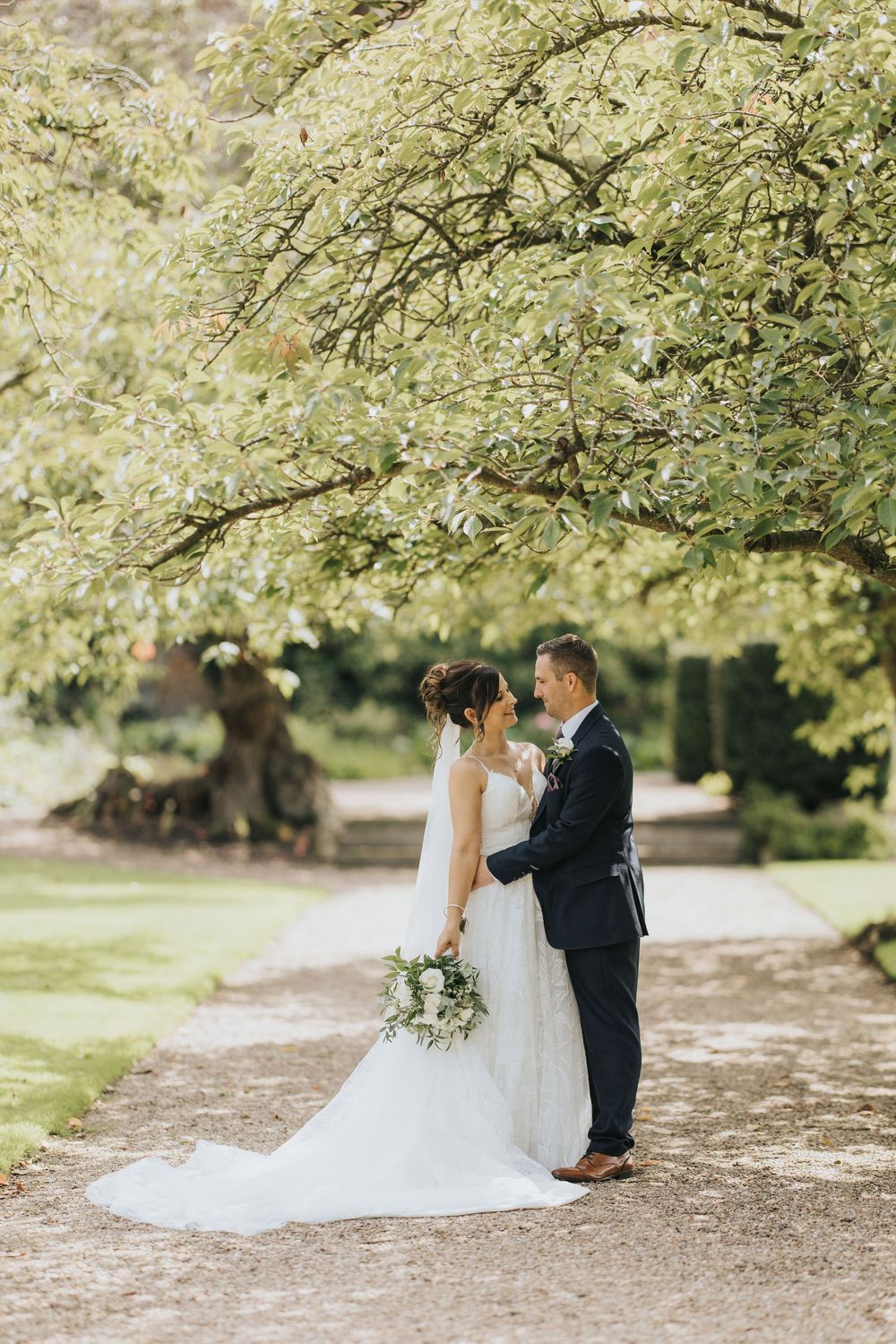 A romantic wedding couple shares intimate moments under blooming trees in a peaceful garden setting.