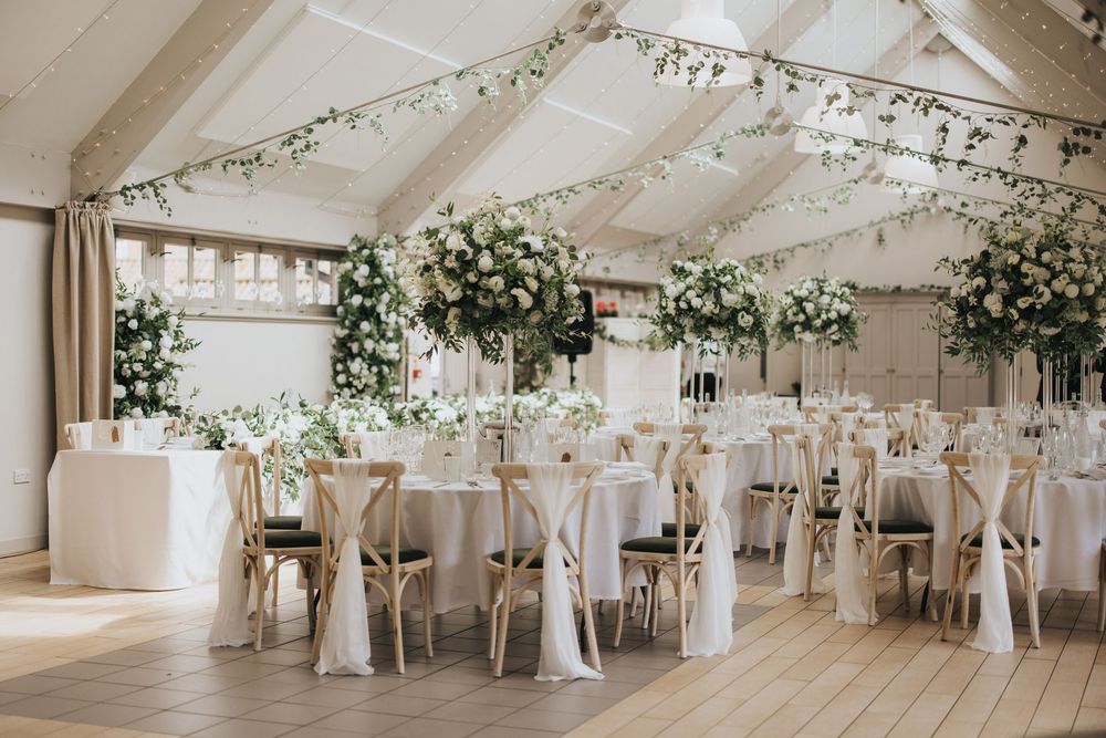 Elegant wedding reception venue with white drapery, floral arrangements and round tables decorated in classic white decor.