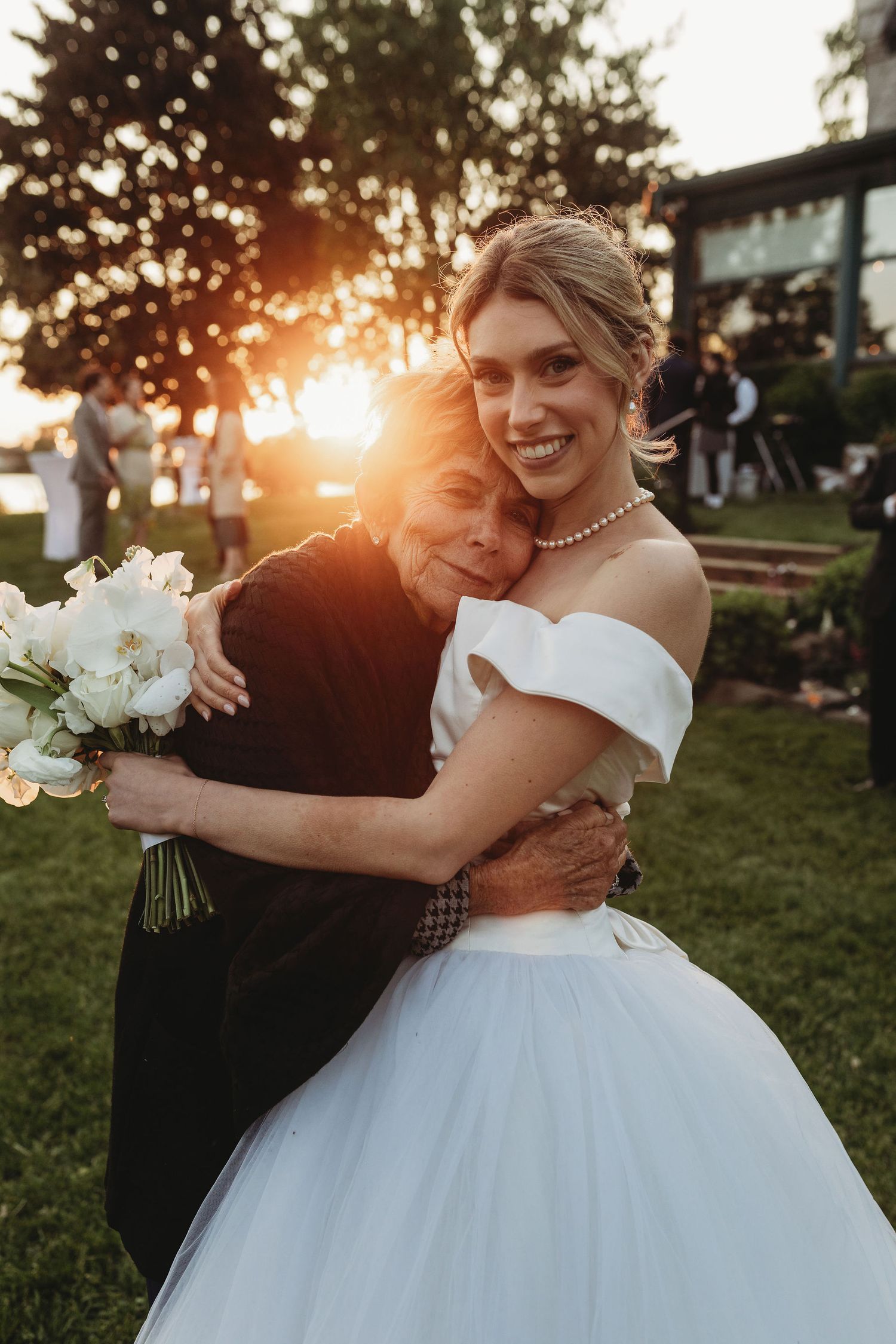 A touching wedding moment captured at sunset with a bride in white dress holding a bouquet during an outdoor celebration.