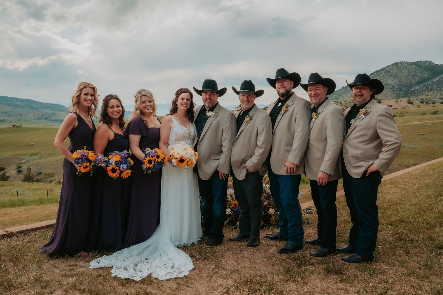 Mountain wedding party with sunflowers poses in Colorado valley against desert landscape at sunset.