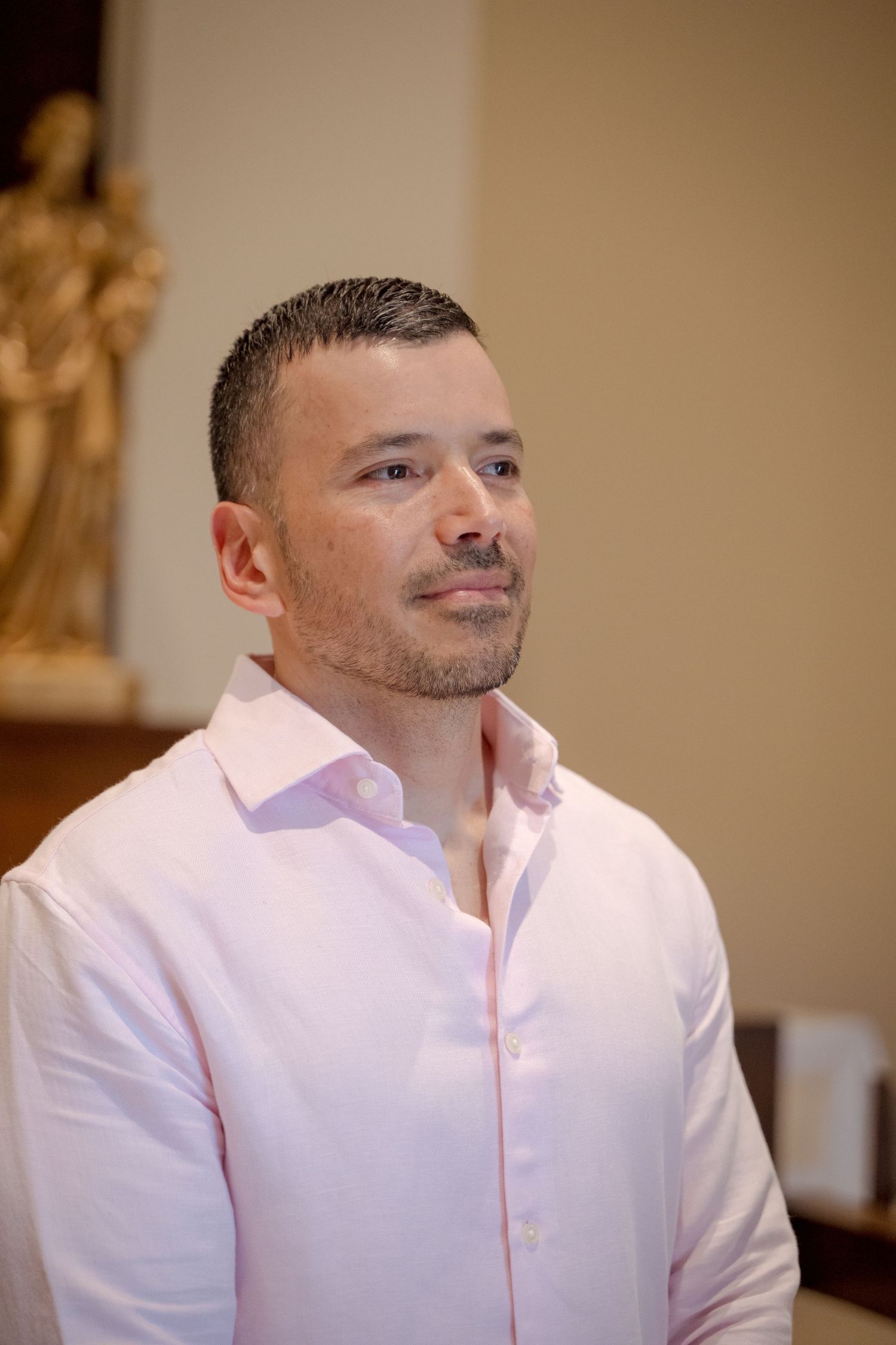 A person in a light pink dress shirt looks contemplatively to the side in an indoor setting.