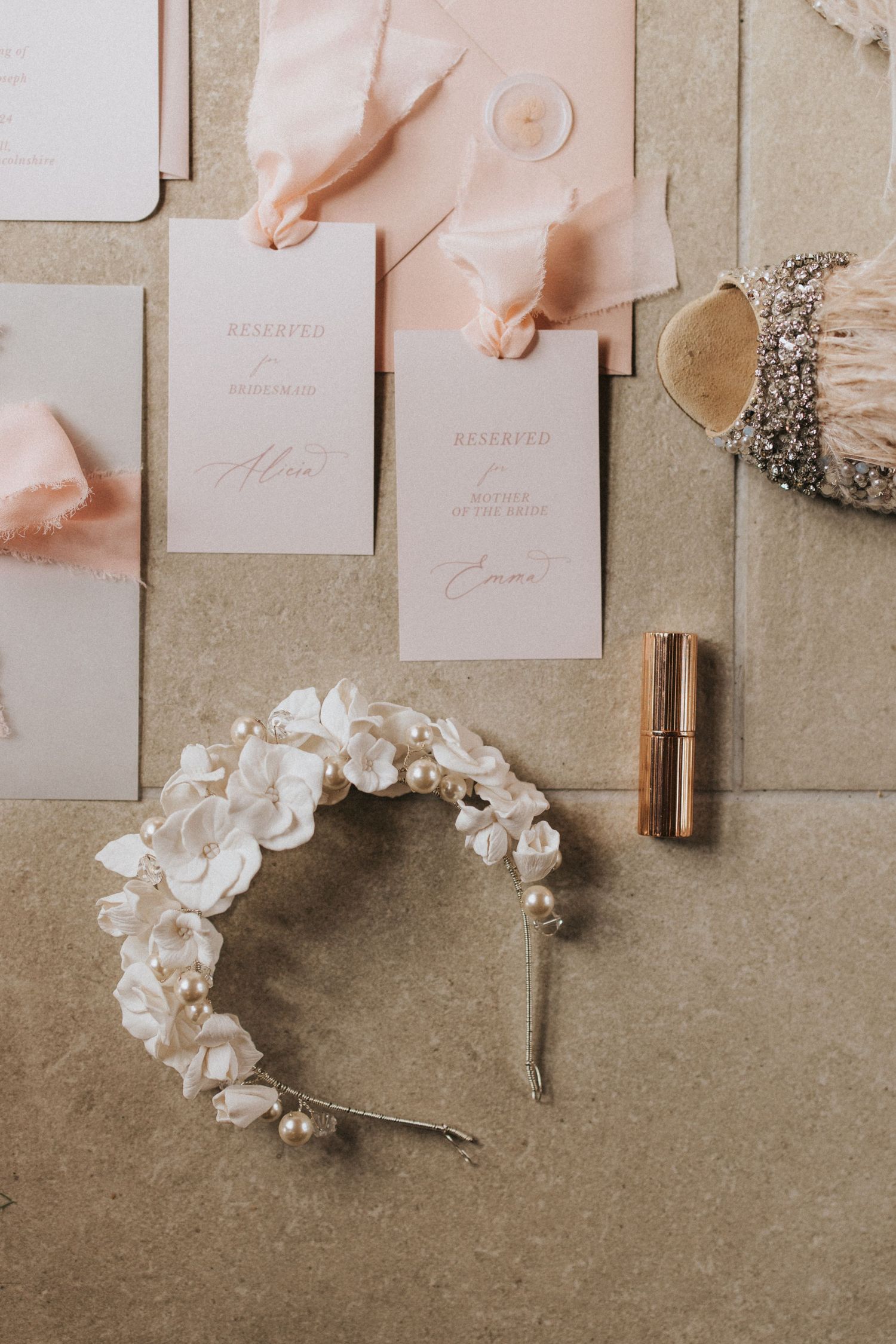 Elegant wedding stationery flatlay with white floral headpiece and blush pink accents on neutral grey background.