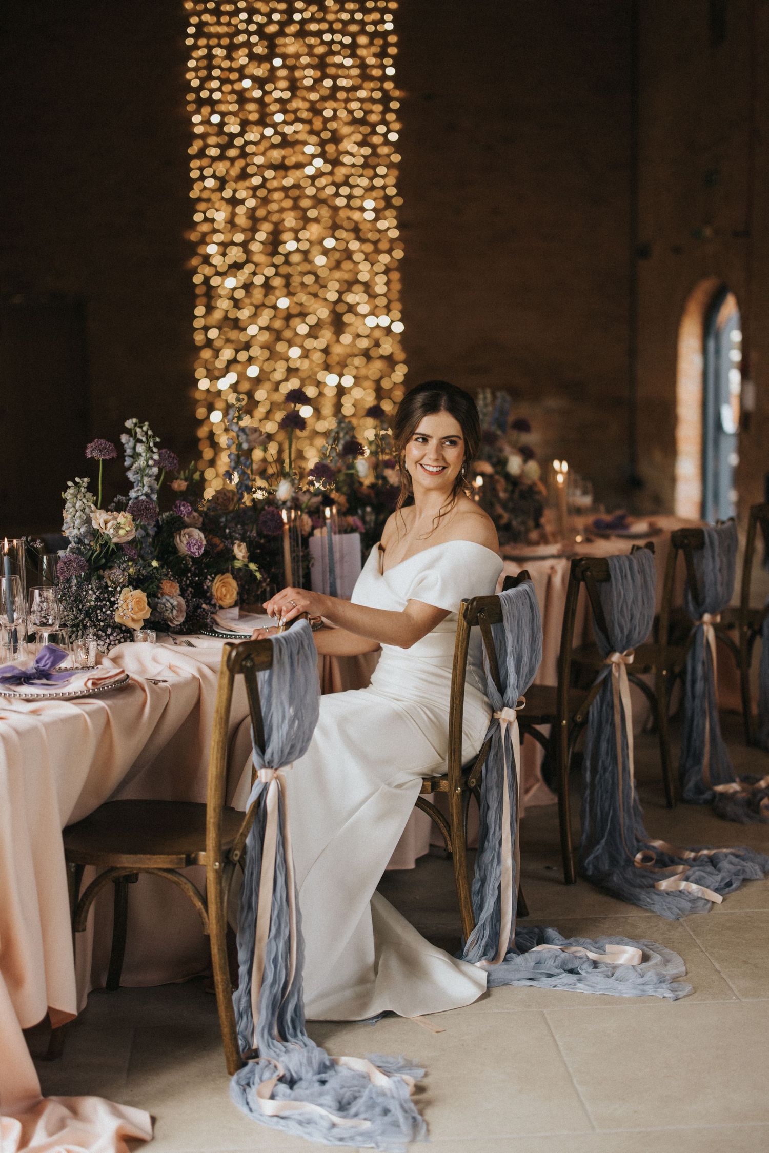 Elegant wedding reception setup with illuminated column, flowing silk decorations and floral arrangements on pastel tablescapes.