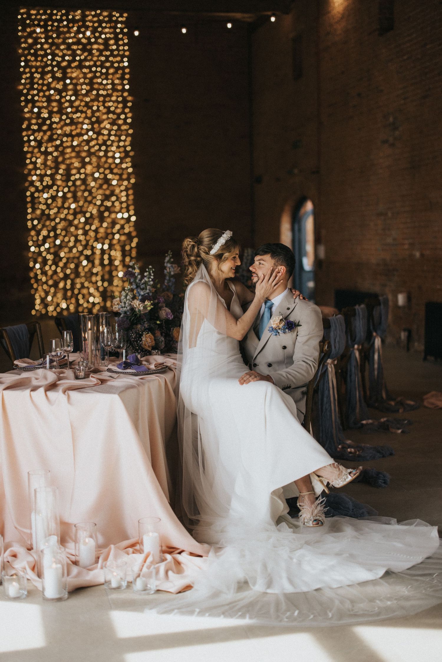 A romantic moment between newlyweds sharing an intimate dance and kiss at their wedding reception venue with twinkle lights.