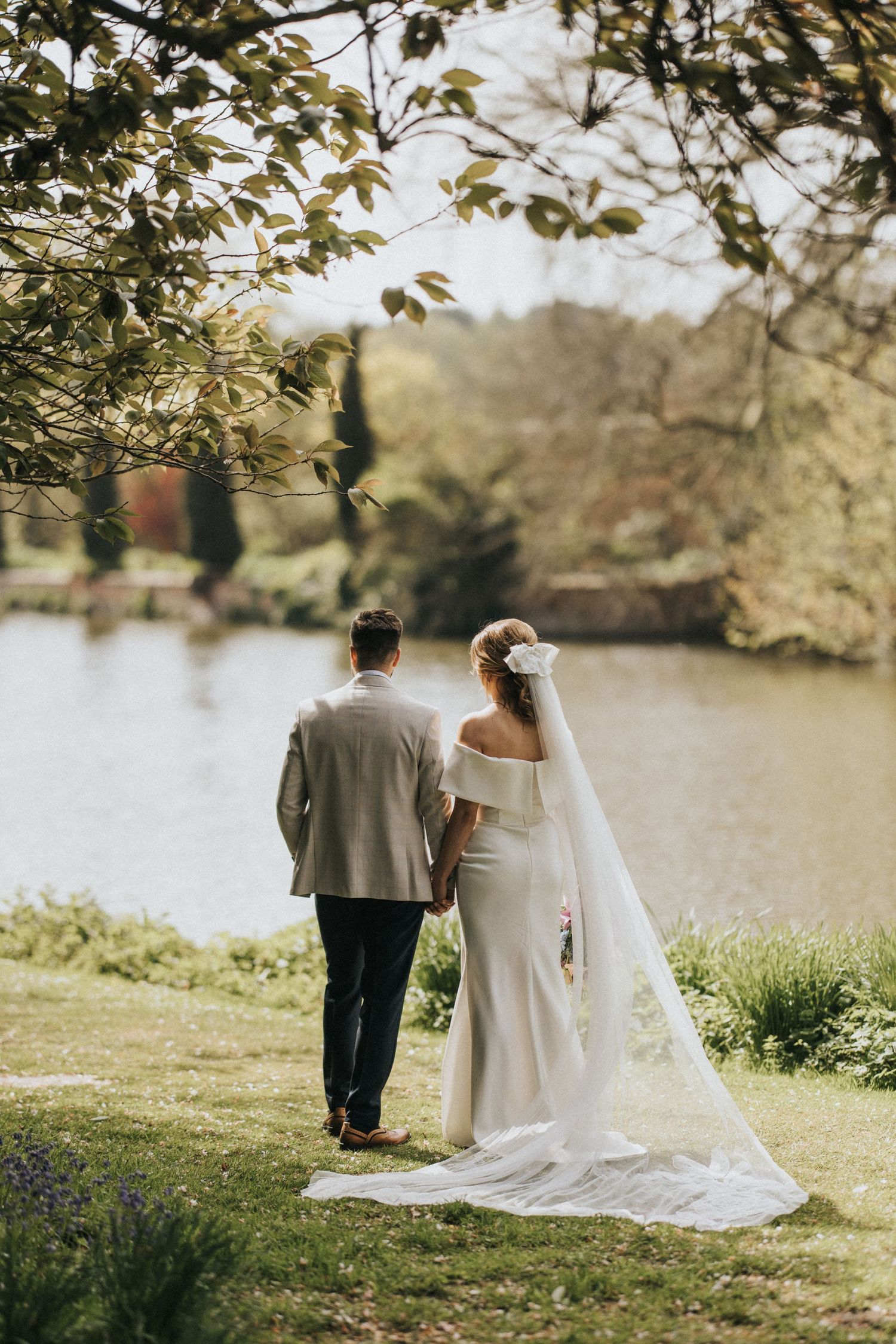 A couple in wedding attire walk along a serene lakeside path in multiple romantic shots during golden hour.