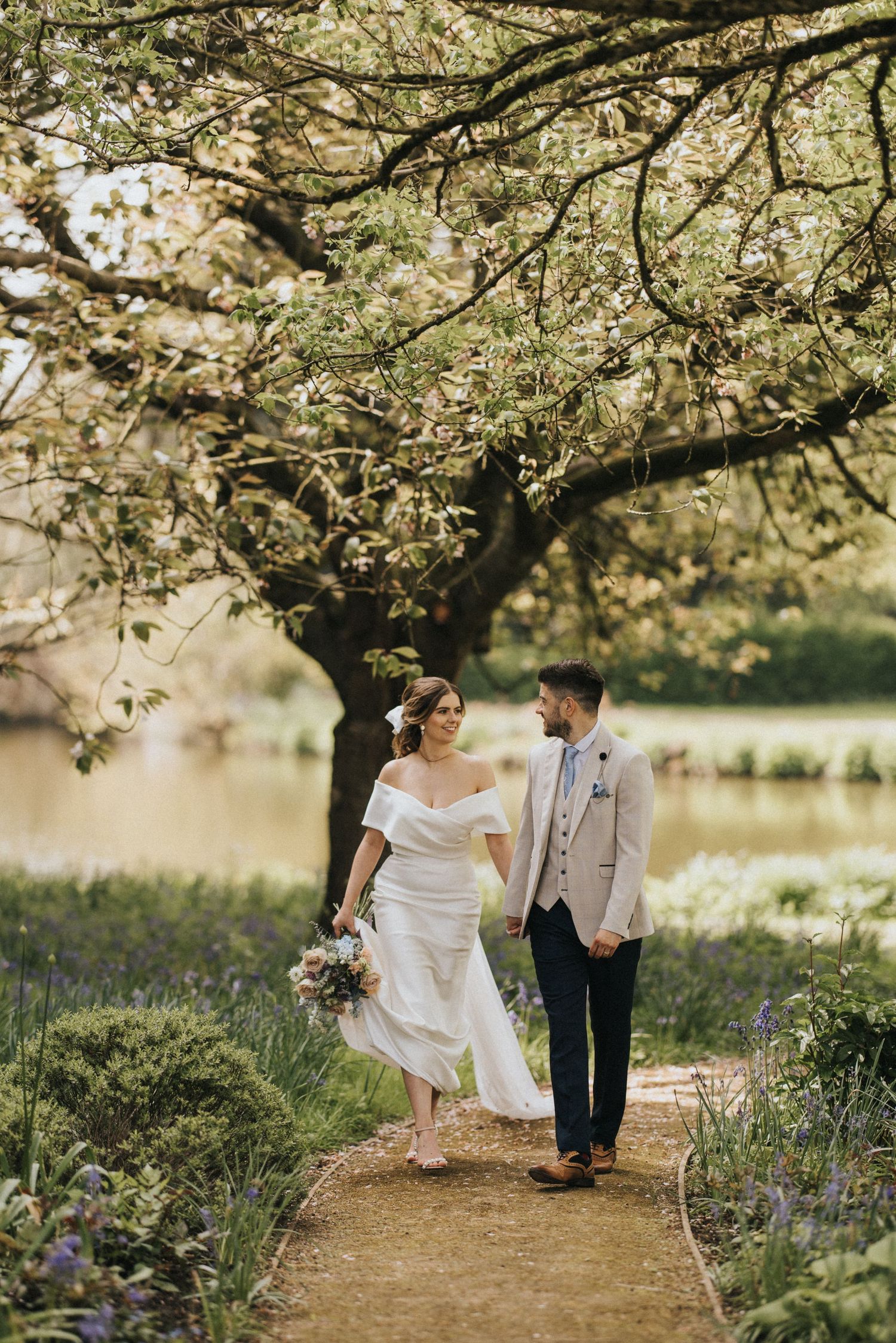 A couple shares a romantic moment under blooming cherry blossoms beside a tranquil lake on a spring afternoon.