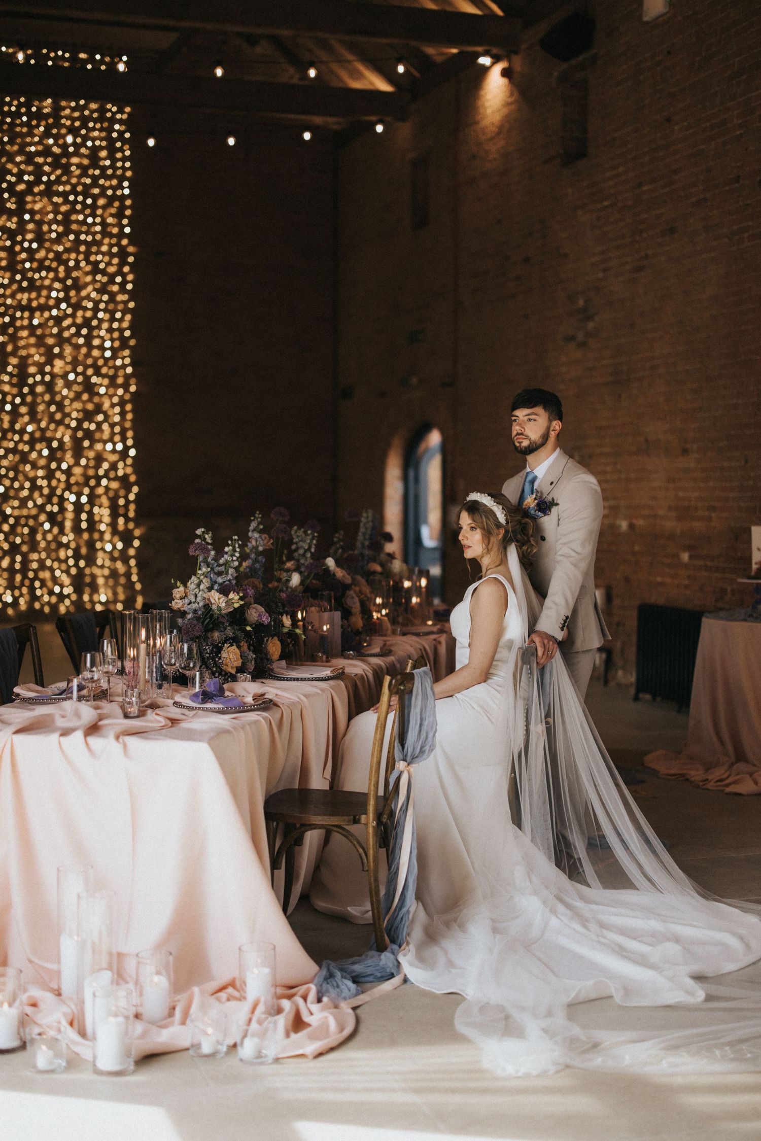 A romantic wedding reception venue with string lights and elegant table settings in a rustic brick room.