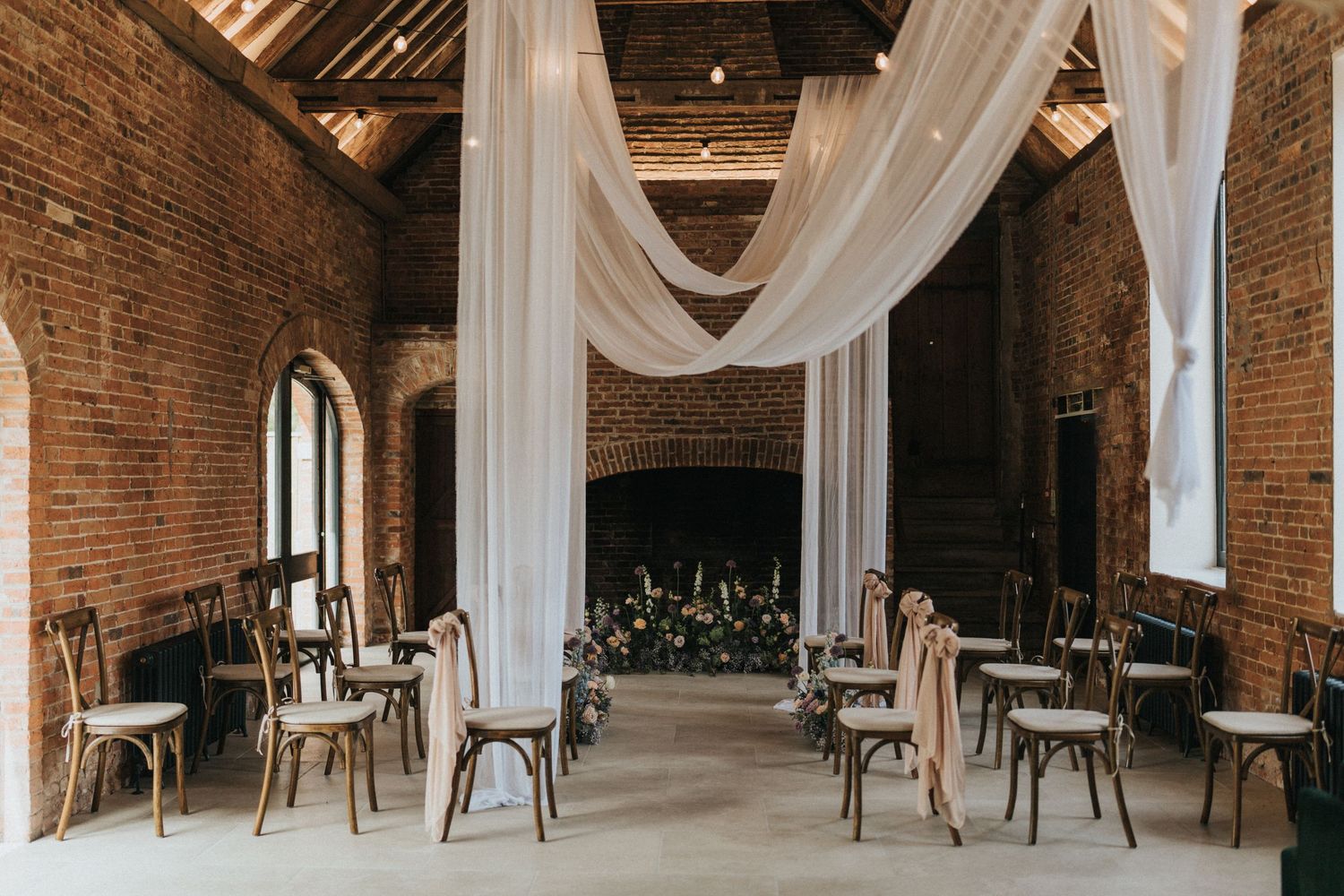 Rustic brick wedding venue with draped white fabric and wooden chairs arranged in ceremony rows.