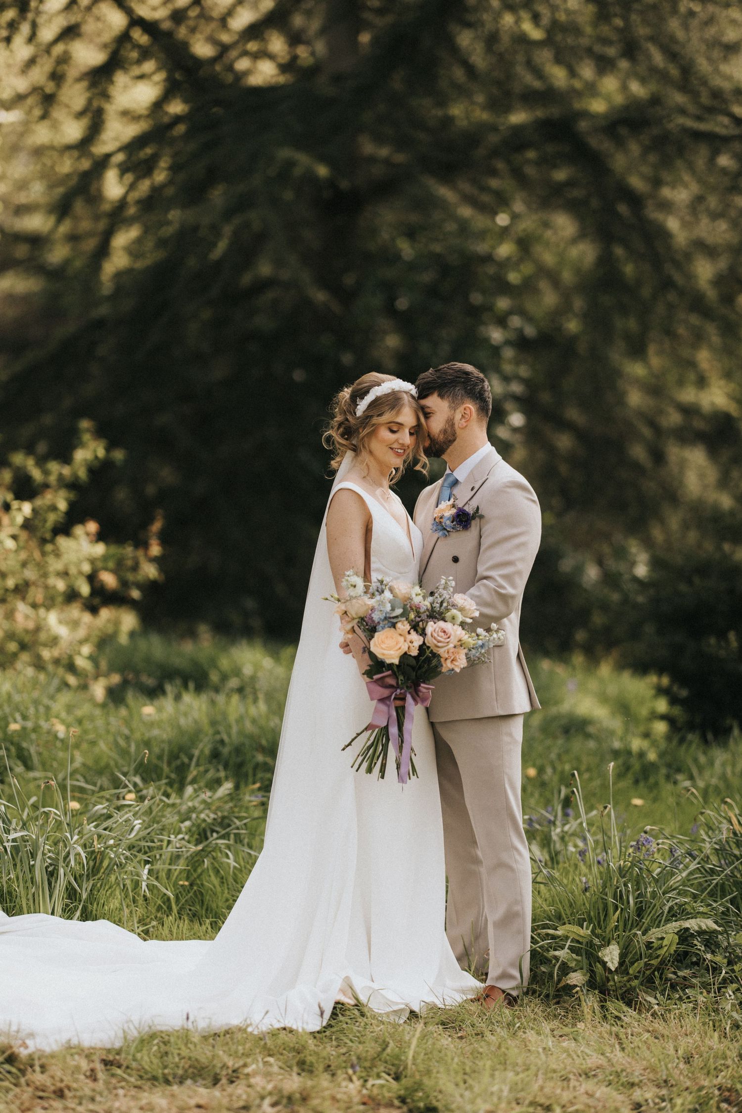A romantic outdoor wedding portrait among tall grass and trees with soft natural lighting.