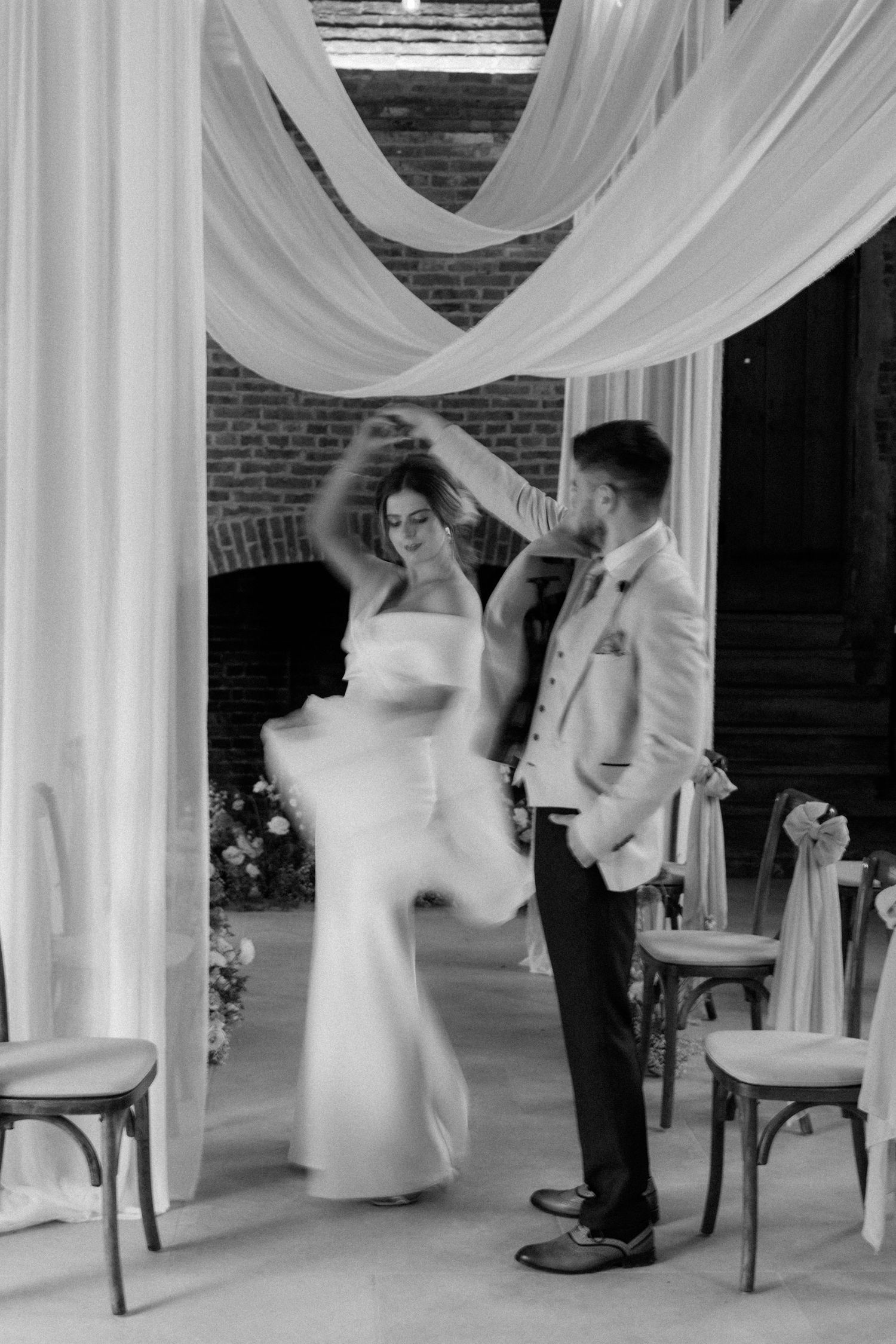 A newlywed couple dancing together beneath elegant white draped fabric at their wedding reception venue.