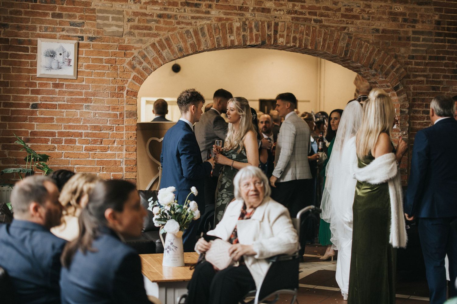 Guests gather and socialize during an event in a rustic brick-walled venue space.