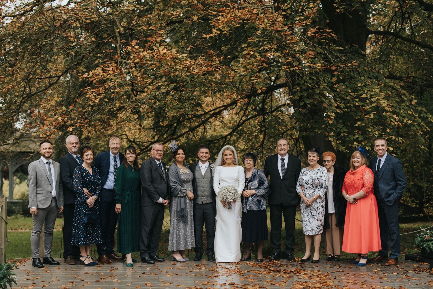 Wedding party poses together under autumn trees with orange and brown leaves on a cloudy fall day.