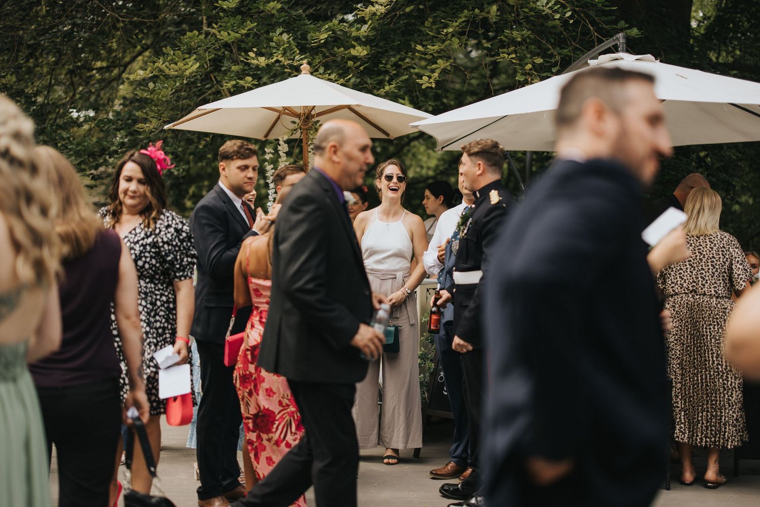 Wedding guests mingle and socialize outdoors under white umbrellas during a summer garden reception.