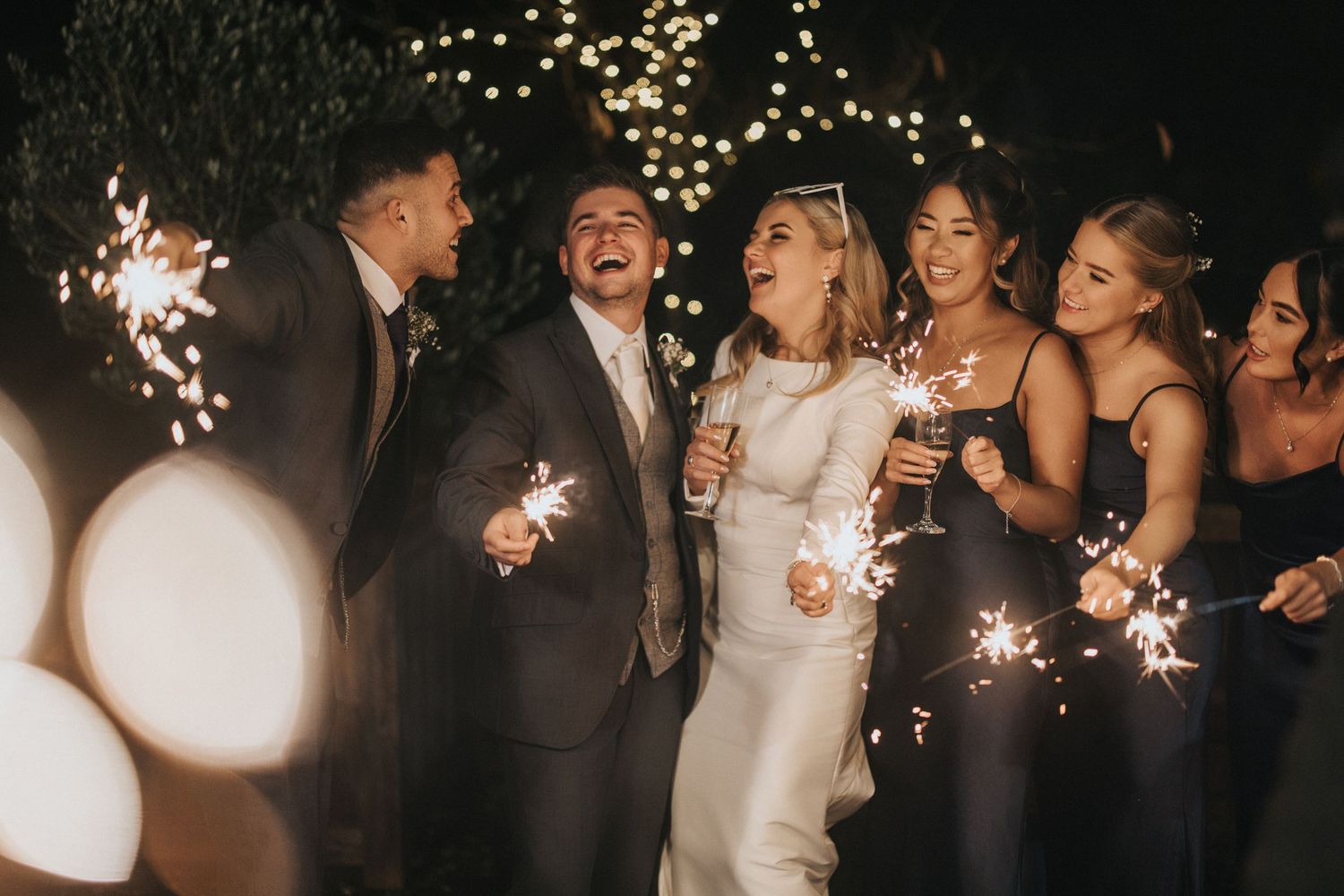 A wedding celebration with sparklers at night showing guests and newlyweds in a joyful dancing atmosphere.