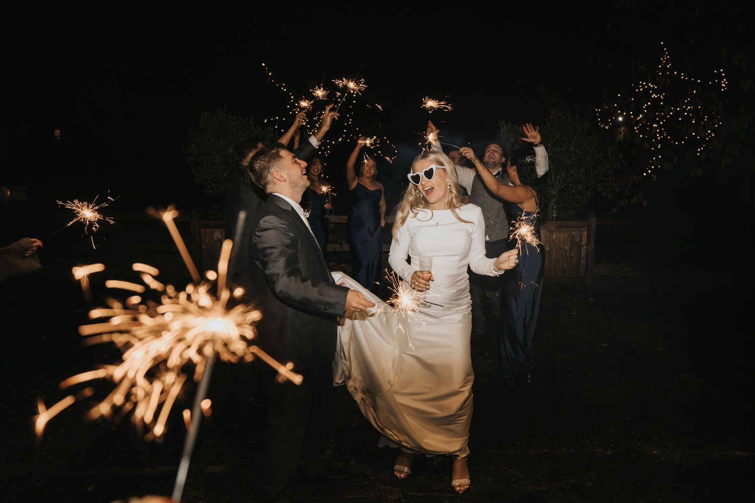 A couple dancing at a nighttime wedding celebration with sparklers illuminating the dark outdoor setting.