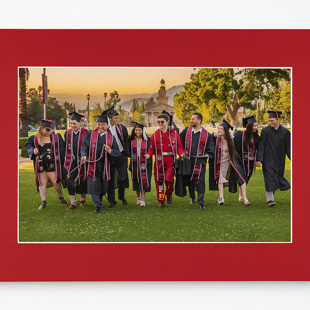 Group of graduates in academic regalia standing together on grass with sunset sky in background during commencement ceremony.