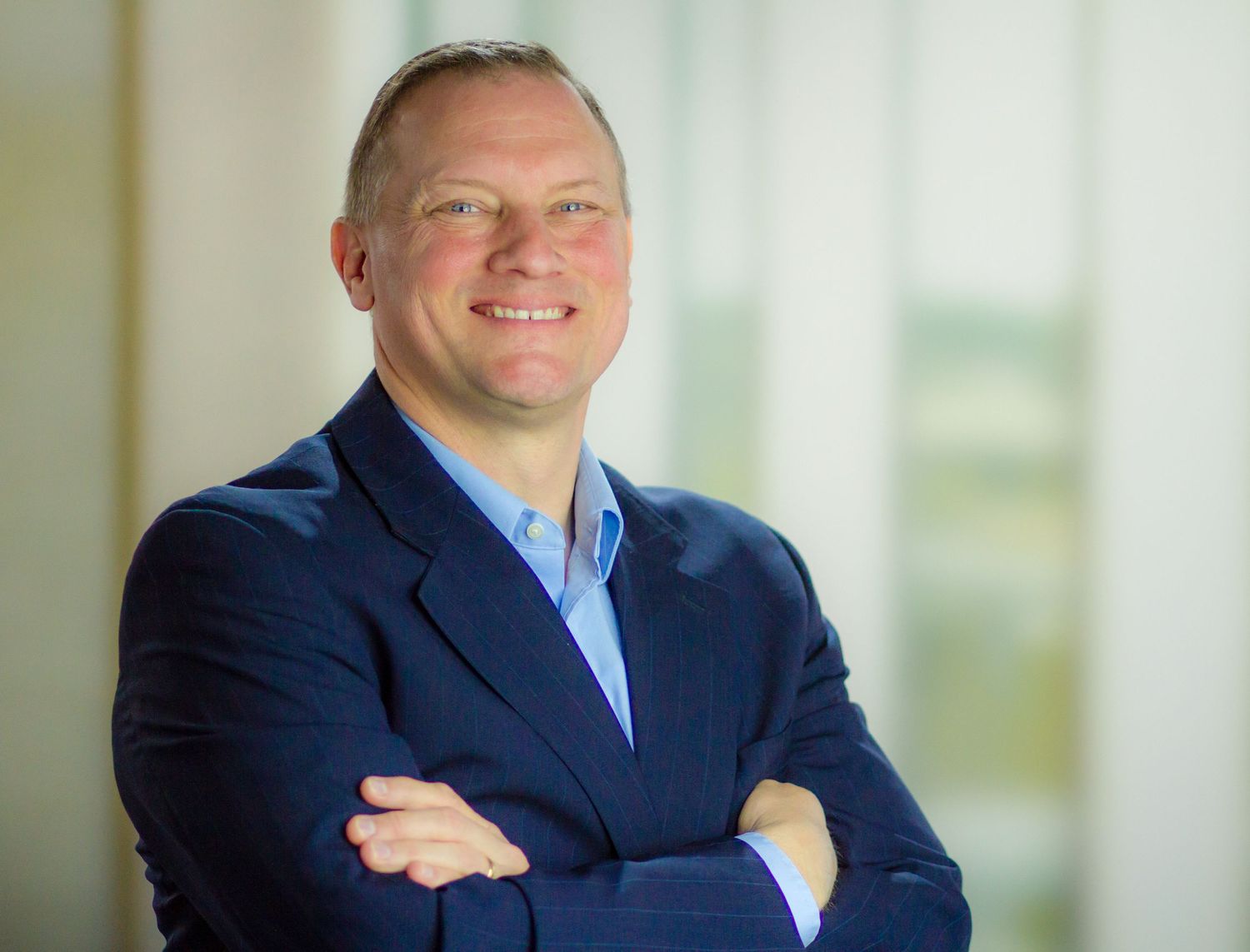 Professional headshot of someone in a navy blazer with crossed arms.
