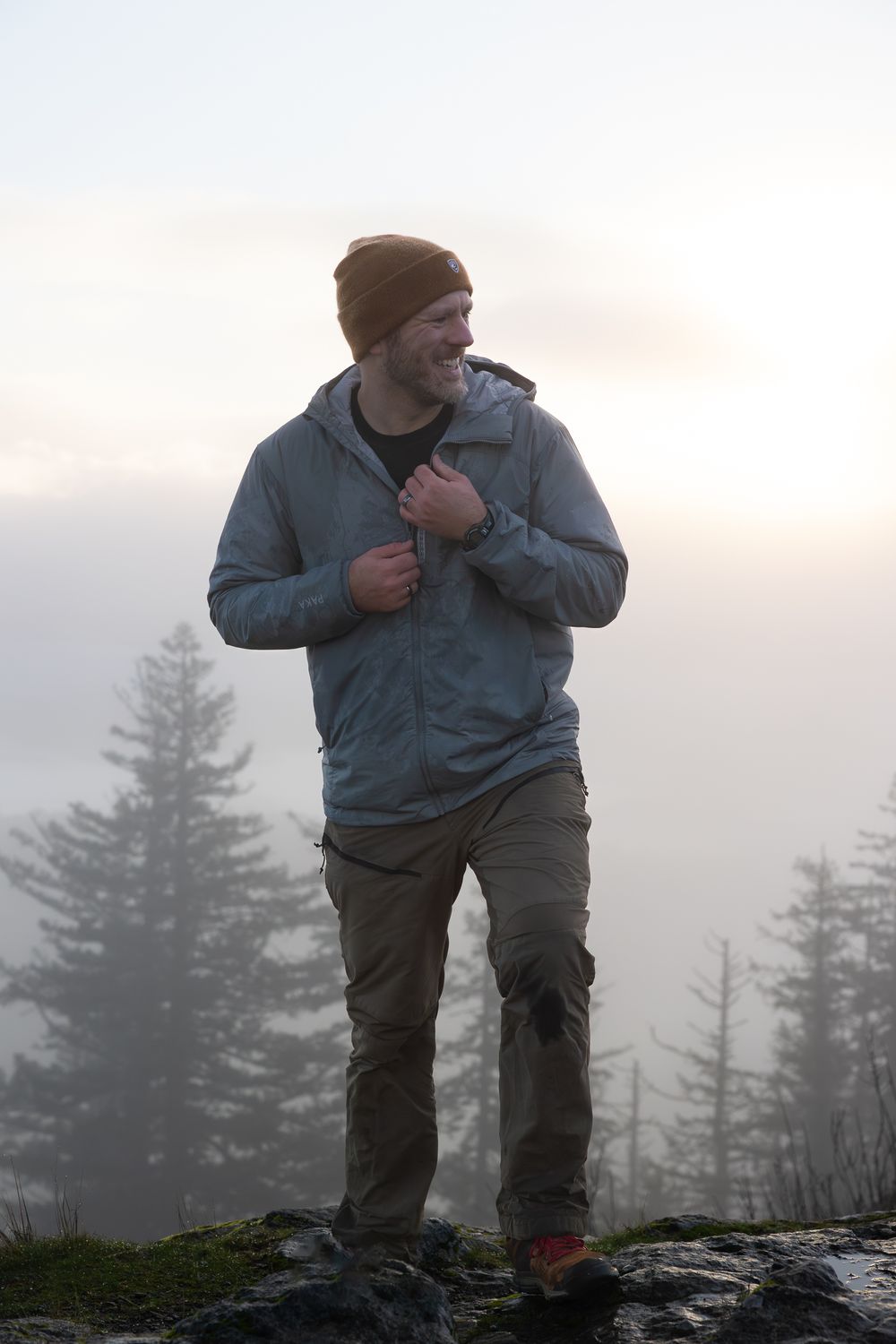 Hiker standing on rocky terrain in foggy mountain conditions wearing outdoor gear.