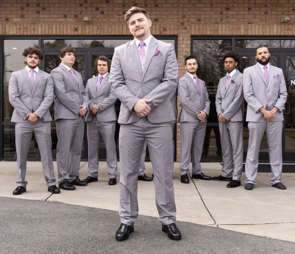Wedding party groomsmen lined up in gray suits outside brick building.