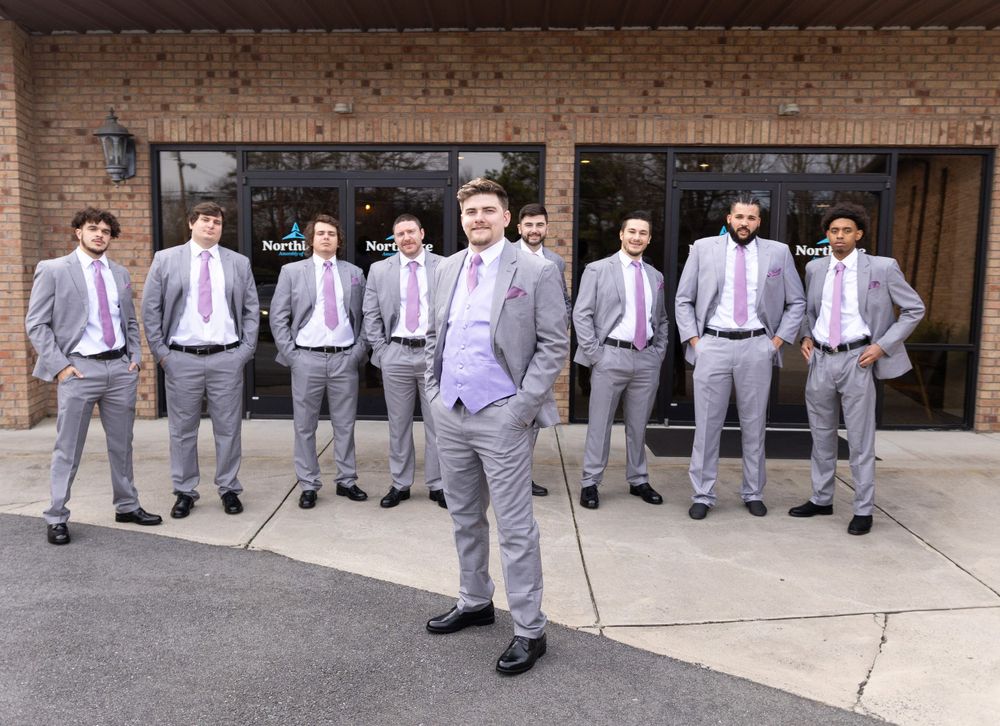 Wedding party groomsmen in coordinated gray suits and pink ties pose outdoors.