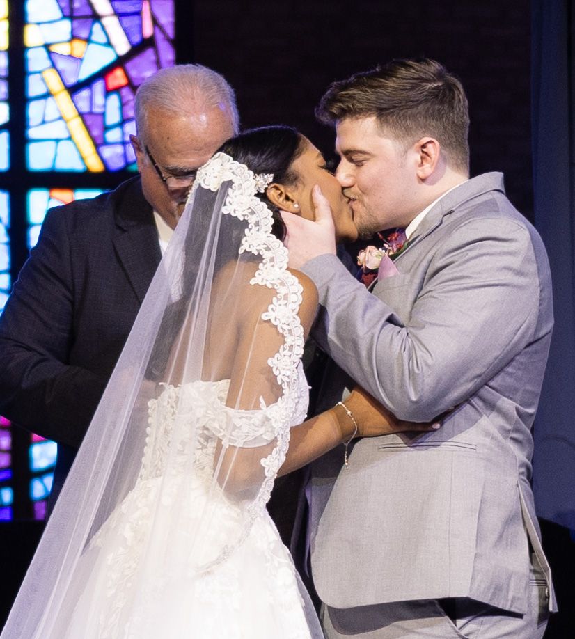 Emotional wedding ceremony moment captured in front of stained glass windows.