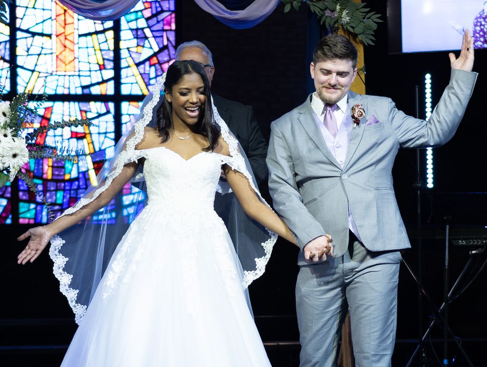Newlyweds celebrate joyfully during wedding ceremony with stained glass backdrop.