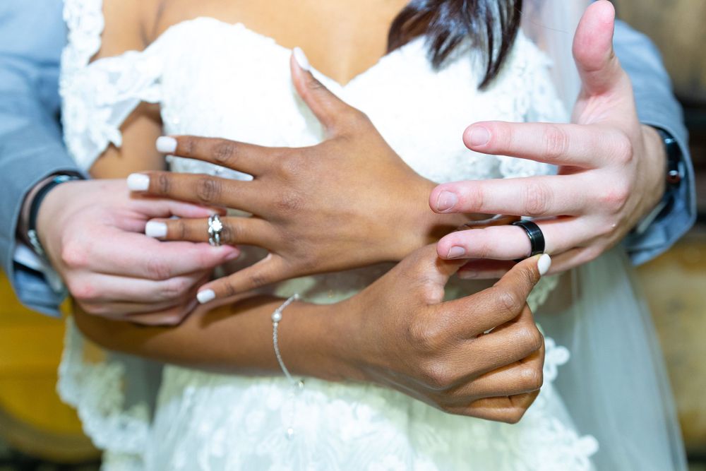 Close-up of newlyweds' hands showing their wedding rings against white dress fabric.