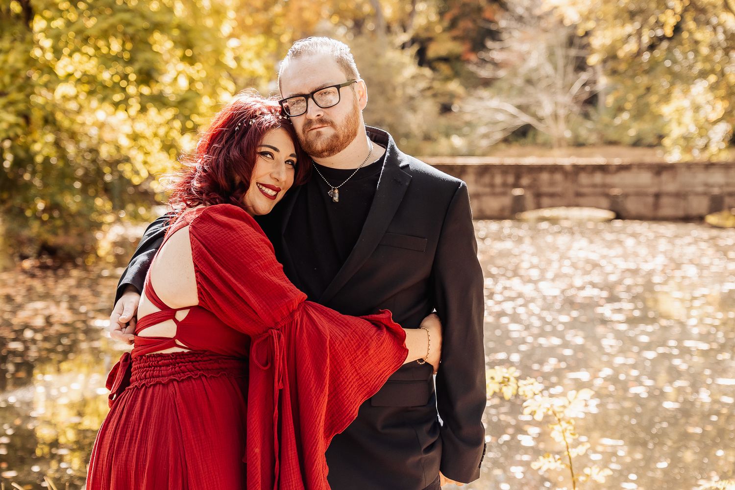 A couple embracing outdoors on an autumn day with golden foliage in the background.