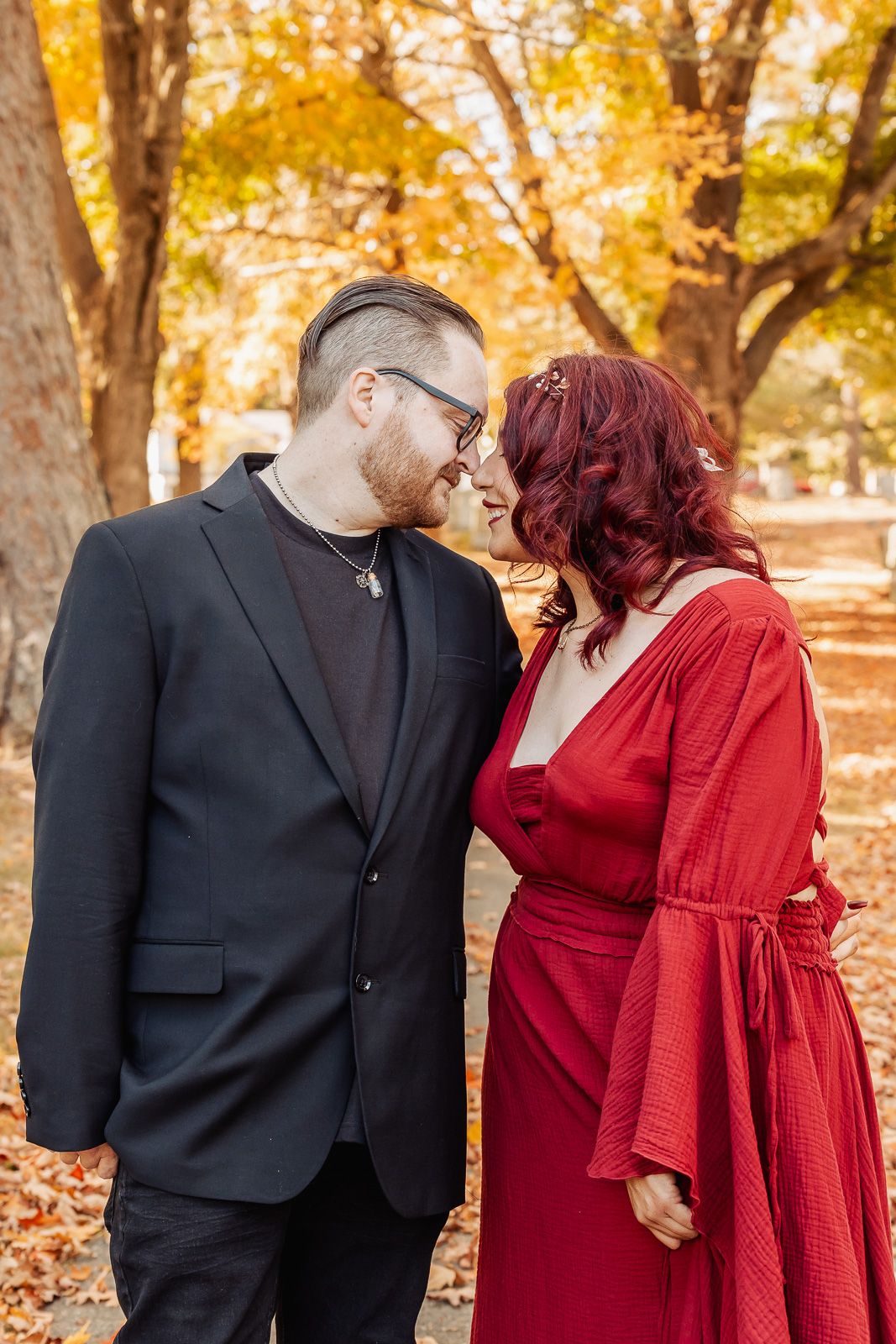 A romantic autumn portrait of a couple with fall foliage, featuring a woman in a red dress.
