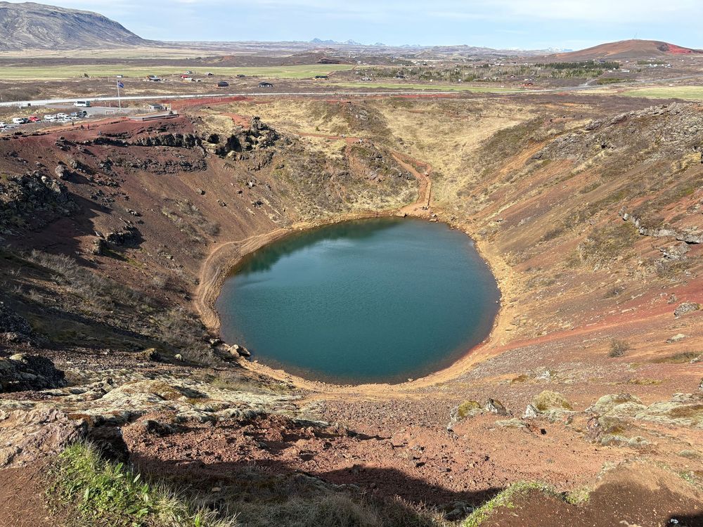 A circular crater lake with turquoise water nestled in volcanic terrain in Iceland's rugged landscape.
