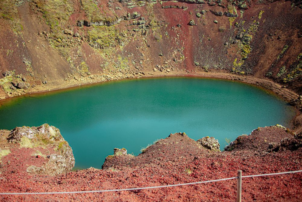 Stunning turquoise lake inside Kerið, a volcanic crater in Iceland with red and green mineral-rich walls.