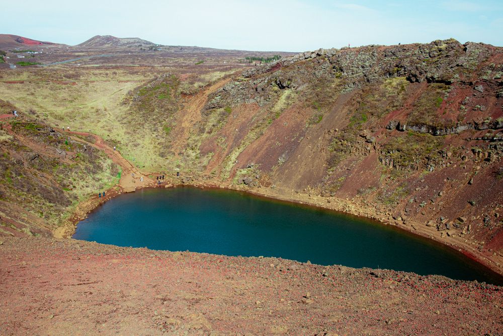 An aerial view of Kerid volcanic crater lake in Iceland surrounded by red volcanic rock and steep walls.