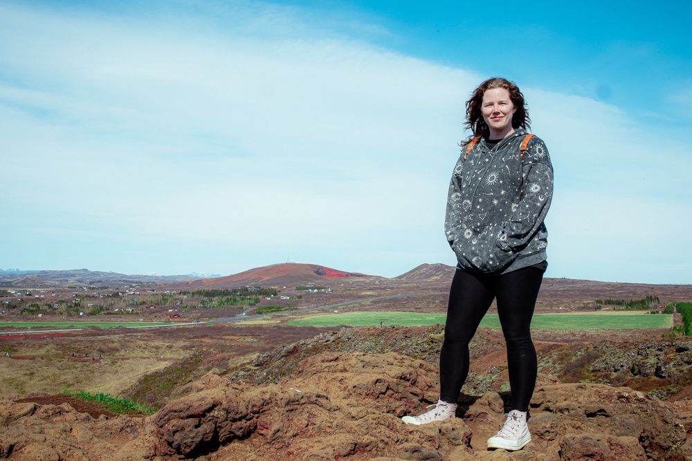 Person enjoying scenic view of rolling hills and mountains against bright blue sky in outdoor landscape.