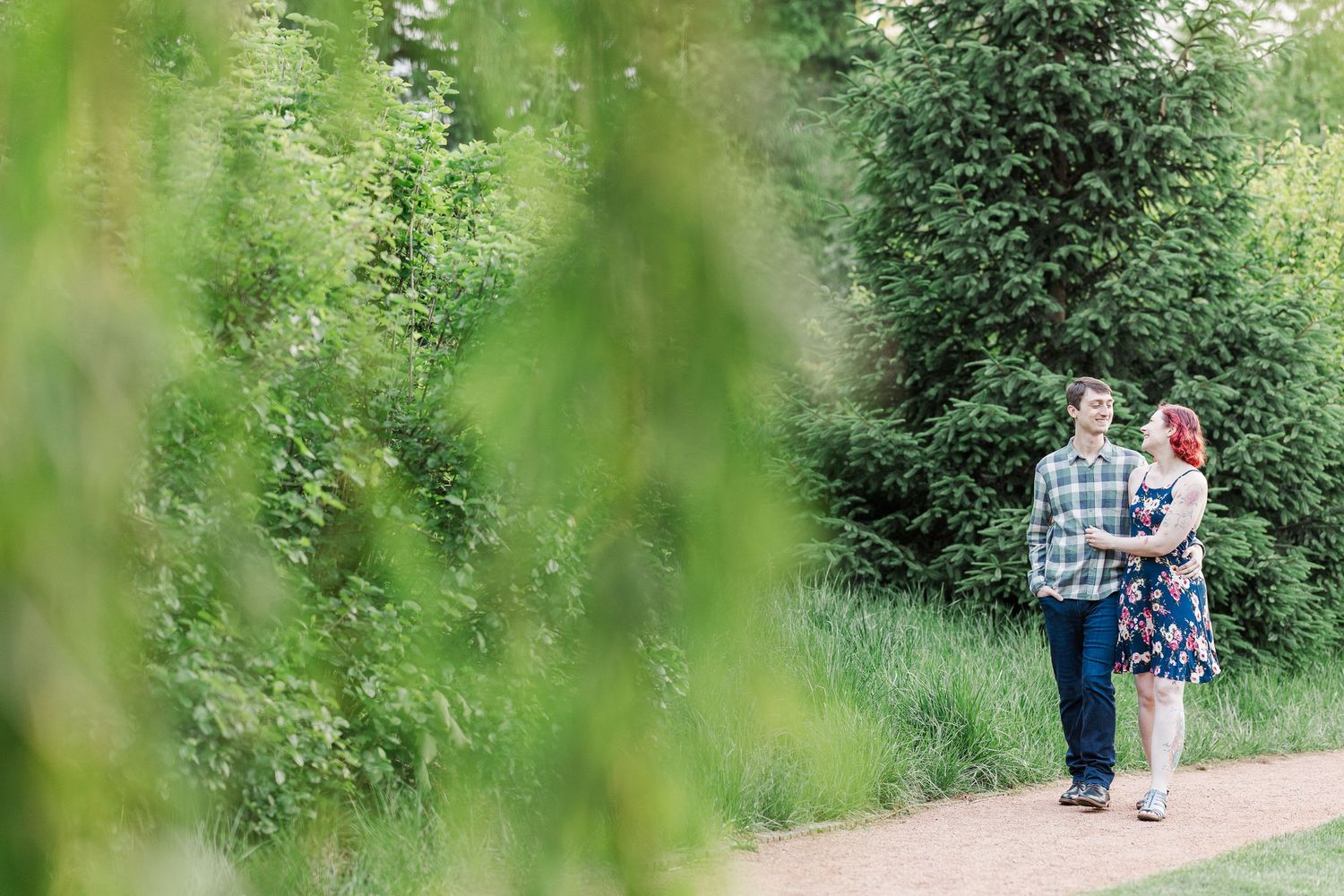 Two people walk together on a dirt path through lush green foliage on a bright summer day at Cantigny Park