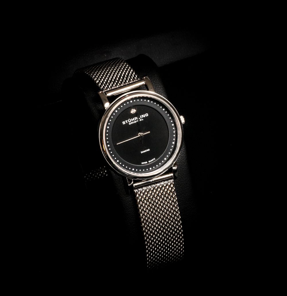 Elegant silver watch with mesh band and black dial photographed in dramatic low-key lighting against dark background.