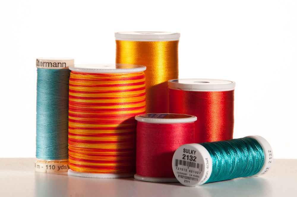 Colorful spools of sewing thread in red, orange, teal and gold arranged on a white surface with natural lighting.