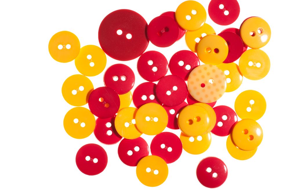 Colorful red and yellow round plastic buttons scattered on a white background.