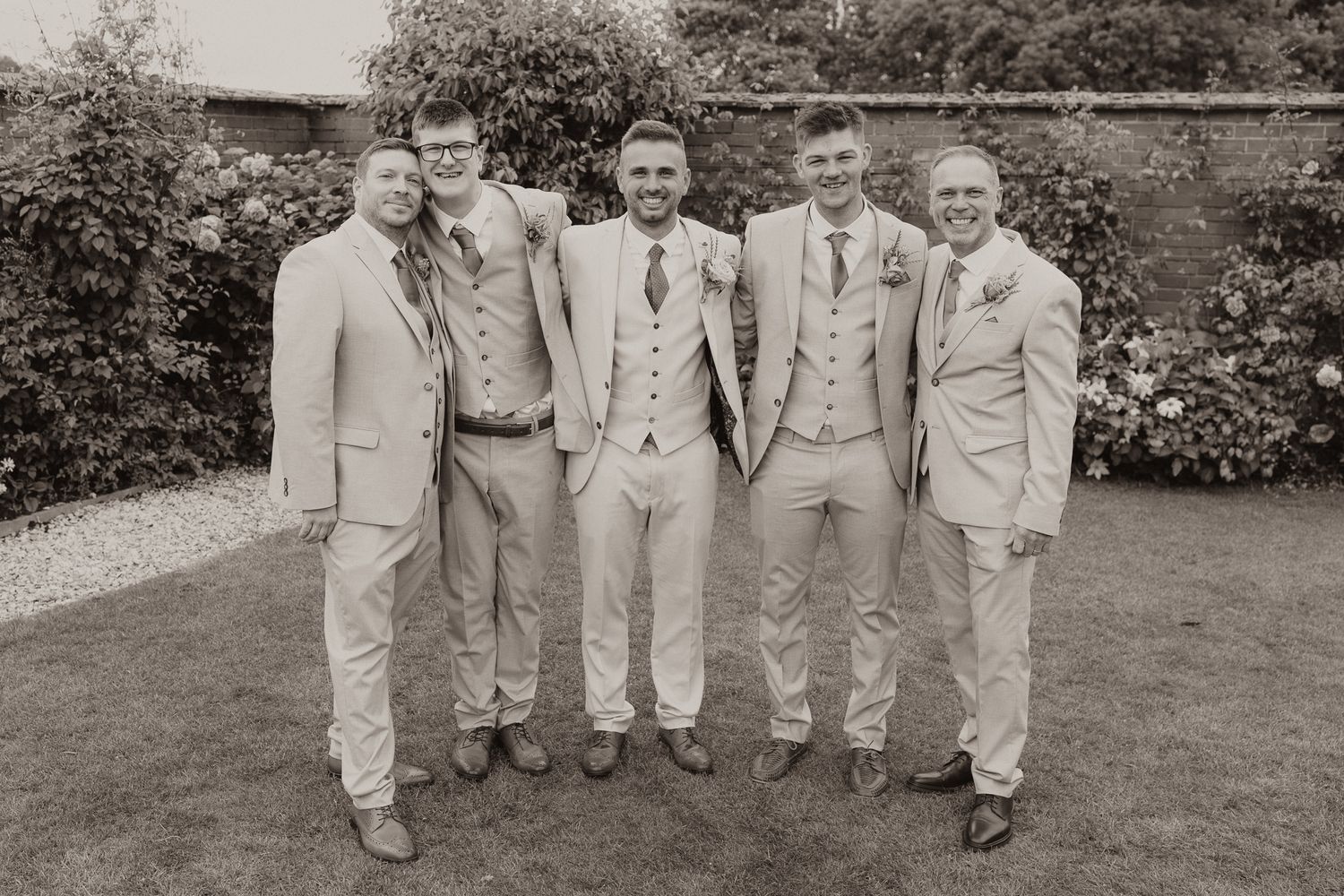 Groomsmen in light colored suits posing together outdoors in black and white photography.
