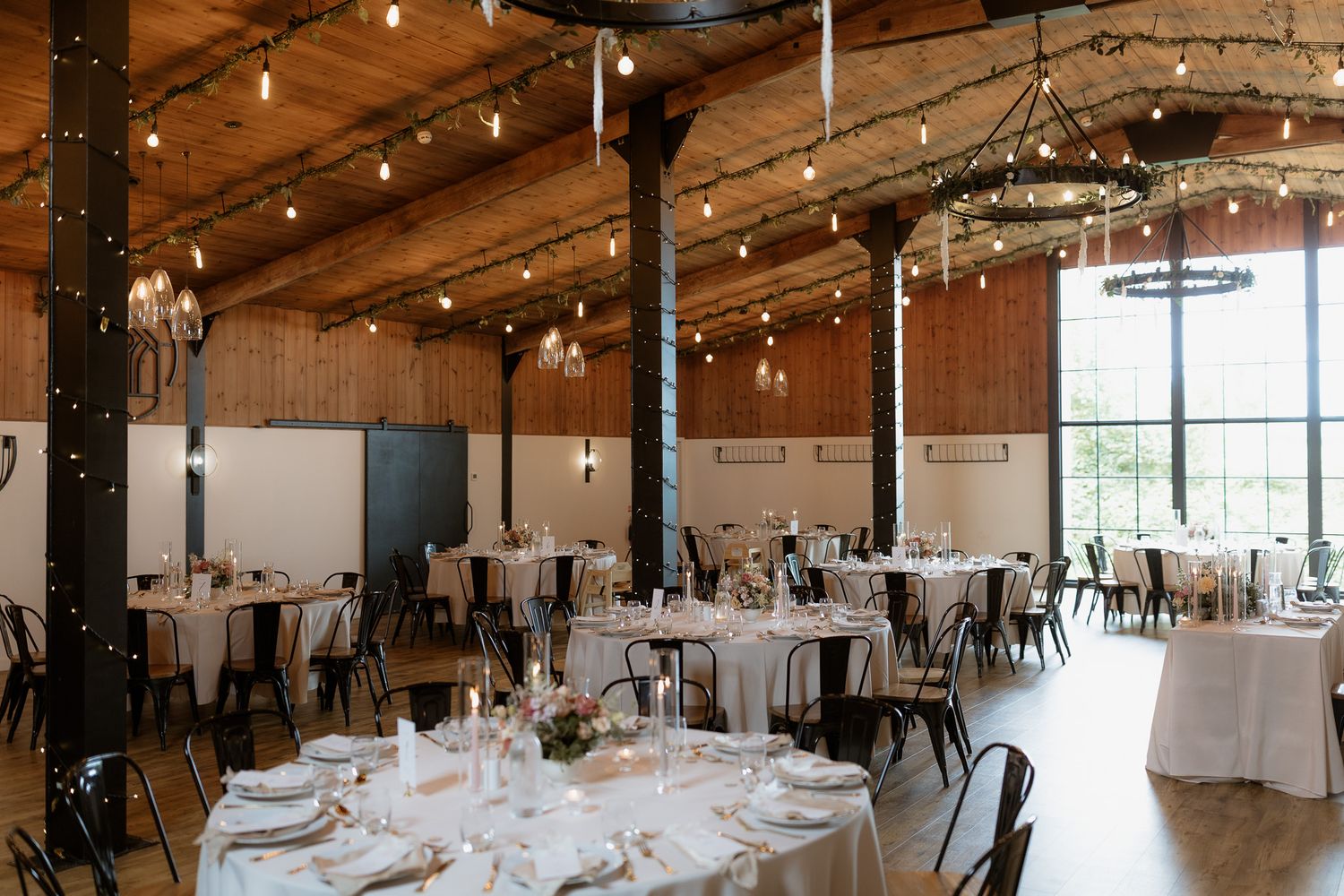 Modern industrial wedding reception venue with exposed beams, string lights and elegant table settings.